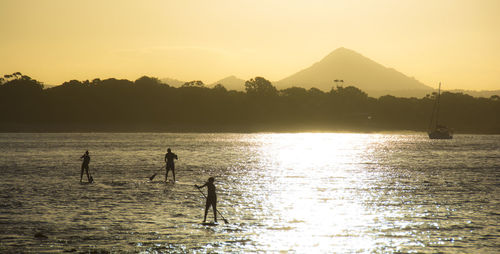 Silhouette people paddleboarding on sea against sky