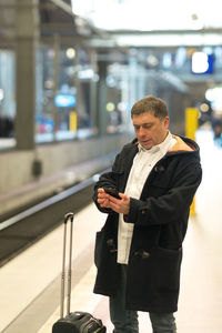 Man using mobile phone while standing at railroad station platform