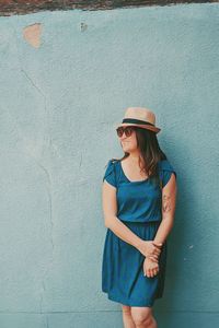 Young woman wearing sunglasses standing against wall