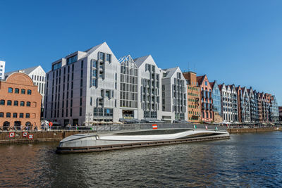Buildings by river against clear blue sky
