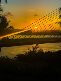 Silhouette bridge over river against sky during sunset