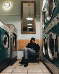 Woman sitting on chair amidst washing machines at laundromat