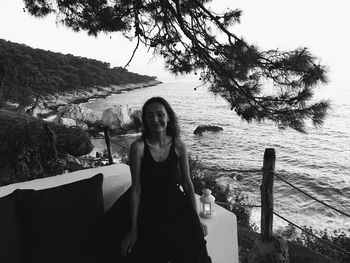 Portrait of smiling young woman standing by tree against sky