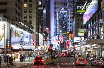 Cars on road amidst illuminated buildings at night