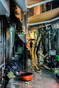 Woman with umbrella on alley amidst buildings in city at night during rainy season