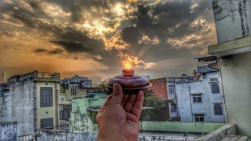 Midsection of person holding umbrella against buildings during sunset