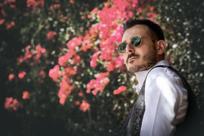 Side view of man wearing sunglasses by flowering tree