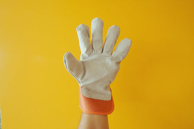 Close-up of hand wearing gloves gesturing against yellow background