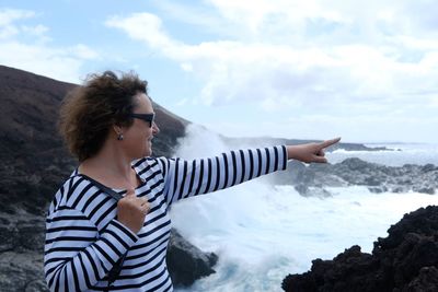 Woman pointing while looking at view of sea standing against sky