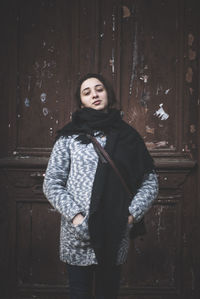Portrait of young woman standing against door in winter