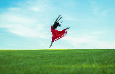 Side view of woman dancing on grassy field against sky