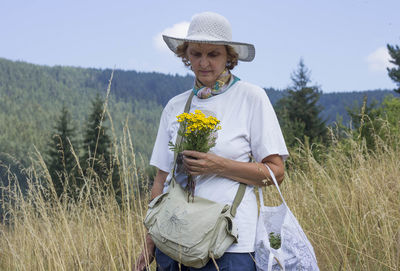 Full length of senior woman standing on field, holding flowers