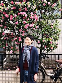 Portrait of smiling young woman standing by flowering plants