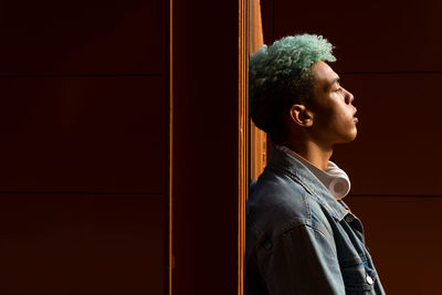 Side view of young man looking away against wall