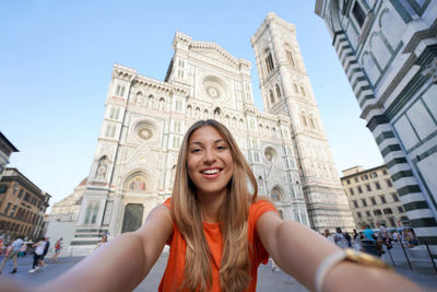 Tourist woman takes selfie smiling at camera in front of the cathedral on sunset in florence, italy