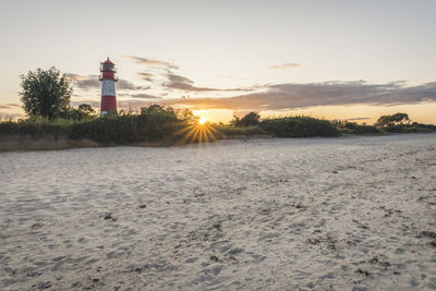 Lighthouse amidst buildings against sky during sunset