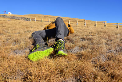 Teenage boy lying on field against clear blue sky