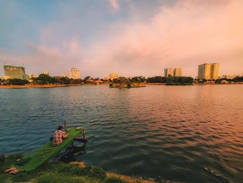 Scenic view of river by buildings against sky during sunset