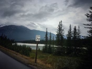 Road sign by trees against sky