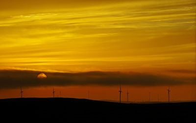 Silhouette windmill on landscape against orange sky