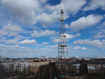 Electricity pylon by buildings in city against sky