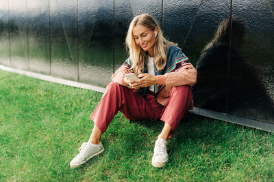 A blonde woman sitting on the lawn uses a mobile phone to communicate social networks. person