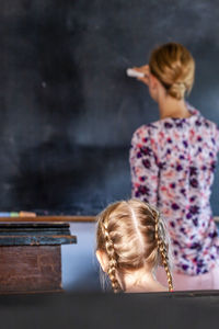 Rear view of teacher teaching female student in classroom