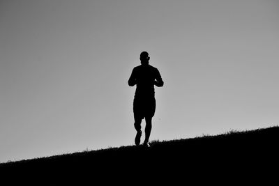 Low angle view of silhouette mid adult man running on field against clear sky during sunset