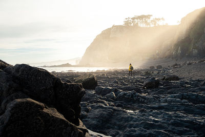 Man standing on rock by sea against sky