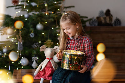 Girl with a gift sits near the christmas tree