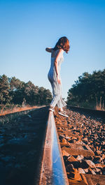 Woman standing by railroad tracks against clear blue sky