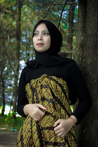 Young woman standing by tree trunk in forest