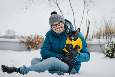 Portrait of man with dog sitting on snow covered field