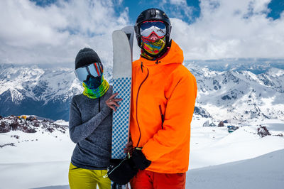 Young couple of skiers man and woman unrecognizable in snowboarding equipment masks on the