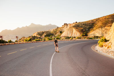 Rear view of man on skateboard on road against mountains