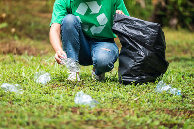 A female activist picking up garbage plastic bottles into a plastic bag in the park for recycling