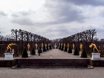 Pathway amidst sculpture in garden against cloudy sky