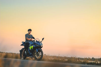 Portrait of man sitting on motorcycle at road against sky during sunset