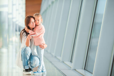 Full length of mother with girl sitting in corridor