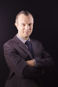 Portrait of businessman with arms crossed standing against black background