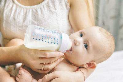 Mother feeding milk to baby through bottle at home