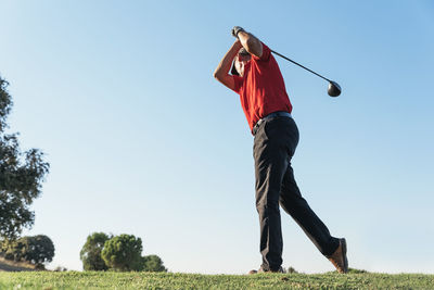 Rear view of man playing with golf club against sky