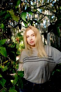 Portrait of confident young woman standing amidst plants at public park