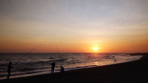 Silhouette people at beach against sky during sunset