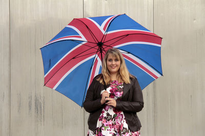 Young woman carrying british flag patterned umbrella against wall