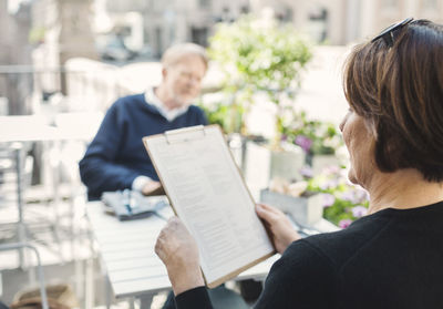 Rear view of woman reading menu while man sitting at sidewalk cafe