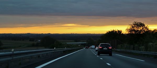 Cars on road against cloudy sky during sunset