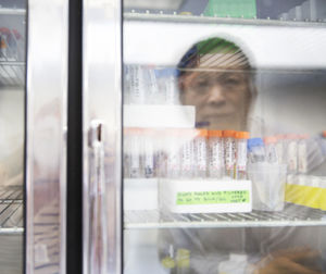 Reflection of senior female scientist in cabinet with test tubes