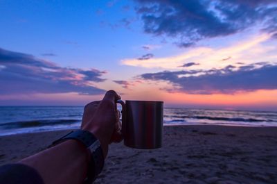 Cropped image of hand holding cup at beach