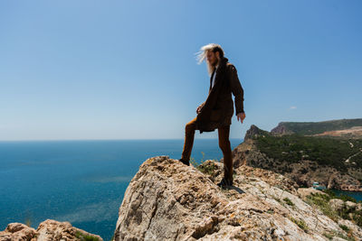 Woman on rock by sea against clear sky